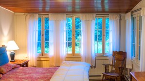 Quarto com cama, poltrona de balanço, cômoda e janela com cortinas.
