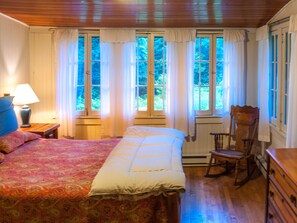 Ein Schlafzimmer mit Bett, Schaukelstuhl, Kommode und einem Fenster mit Vorhängen.