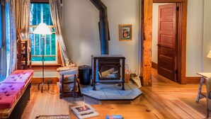 A cozy living room with a fireplace, a sofa, a table with books, and a window with curtains.