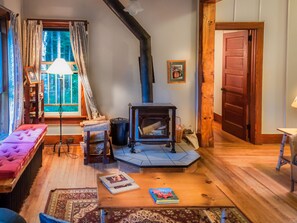 Een gezellige woonkamer met een open haard, een bank, een tafel met boeken en een raam met gordijnen.