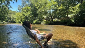 A person sitting in a chair partially submerged in a river, surrounded by greenery and trees.