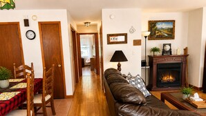 A living room with a fireplace, a sofa, a dining table with chairs, and a hallway leading to another room.