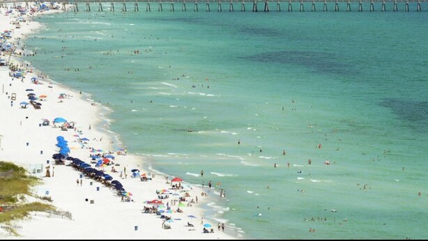 A beach with a pier extending into the ocean, surrounded by a city skyline. - A good morning of sunshine begins with you being here, so why wait to come down? (Panama City Beach)