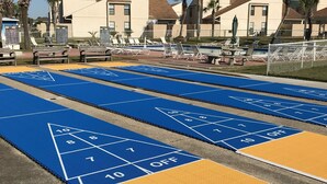 A hotel courtyard with a shuffleboard court, lounge chairs, and a pool area. - A good morning of sunshine begins with you being here, so why wait to come down? (Panama City Beach)