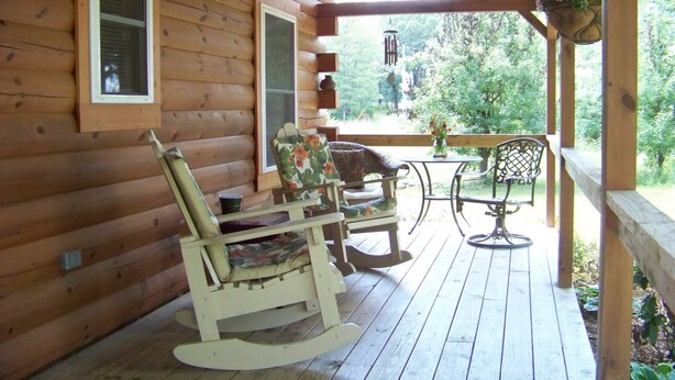 A wooden cabin with a porch featuring rocking chairs, a table, and hanging flower baskets.