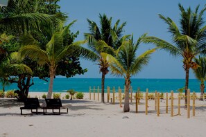 Una playa con palmeras, una valla de madera y dos sillas reclinables negras.