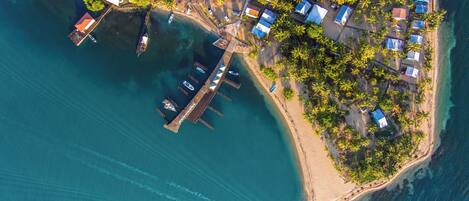An aerial view of a coastal area with a dock, boats, and a small settlement with houses and trees.