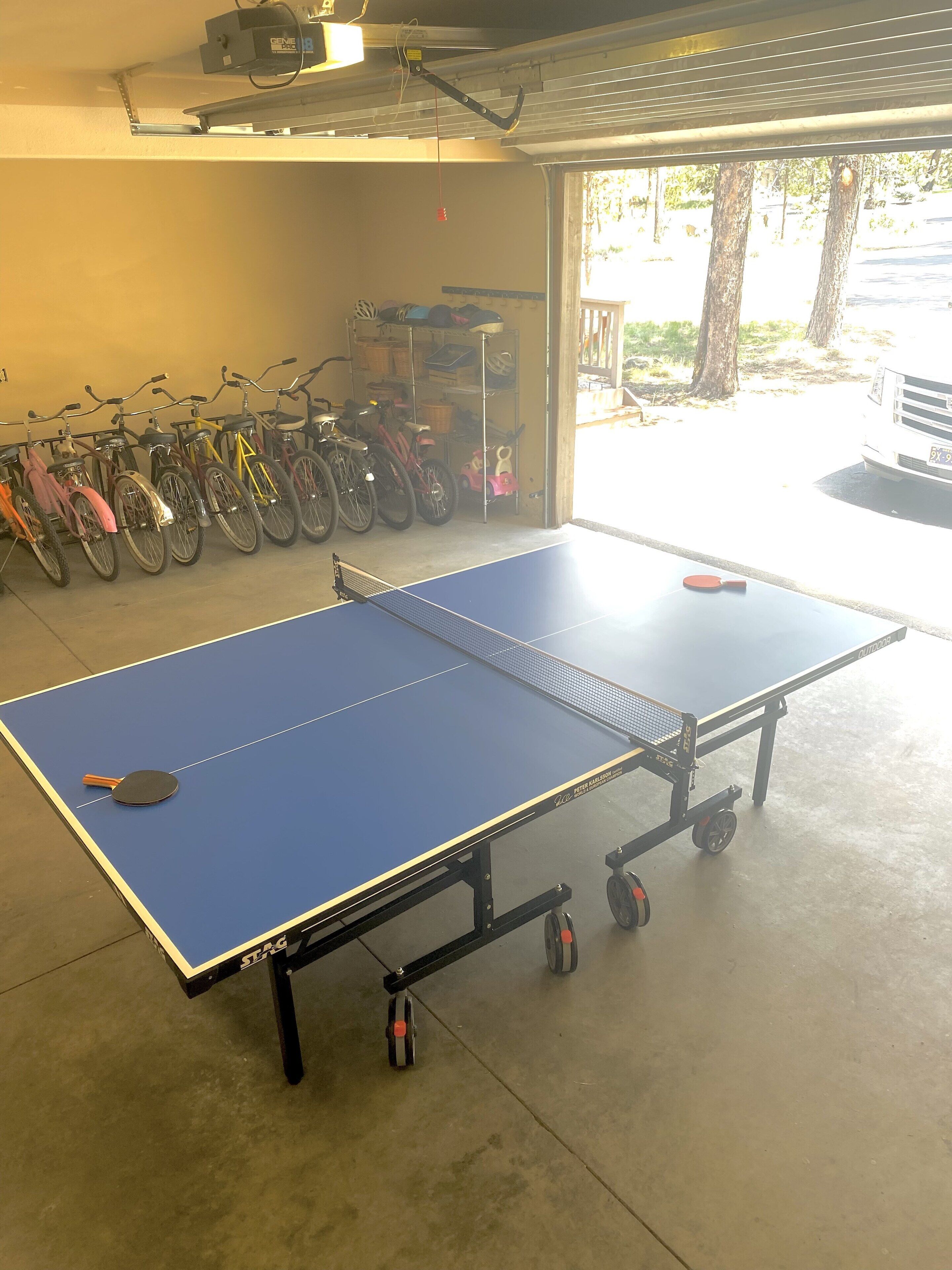 A ping pong table in a garage with bicycles in the background.
