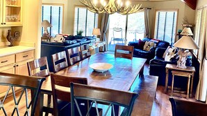 A spacious dining area with a large wooden table and chairs, a chandelier, and a ceiling fan. - 5-bedroom vacation home steps to the Deschutes River (Sunriver)
