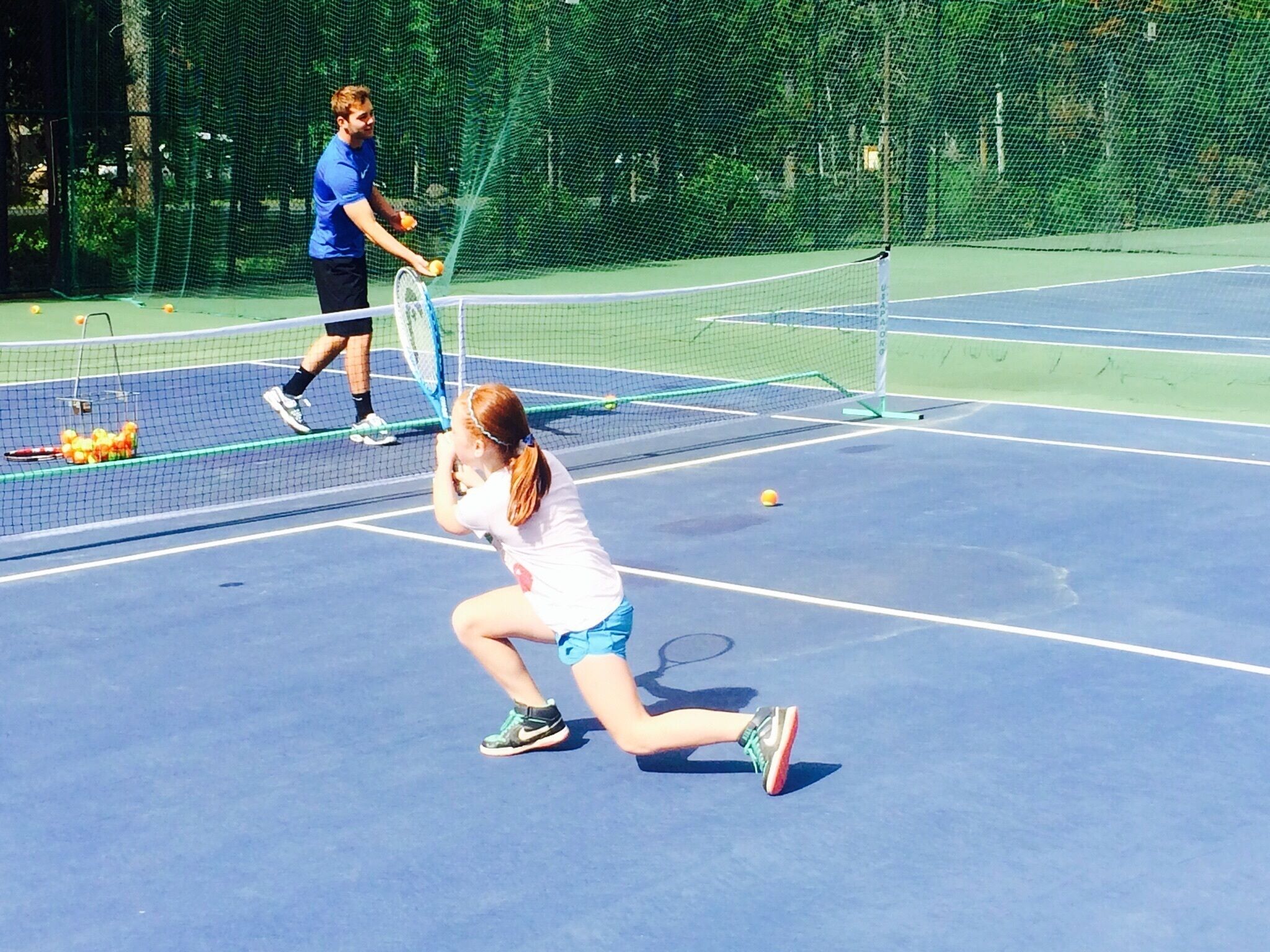 Een tennisbaan met een net, een speler in een wit shirt en blauwe korte broek, en een andere speler in een blauw shirt en zwarte korte broek.