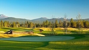 A golf course with a flag, trees, and mountains in the background. - 5-bedroom vacation home steps to the Deschutes River (Sunriver)