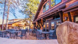 An outdoor patio with metal tables and chairs, a wooden deck, and a large rock in the foreground. - 5-bedroom vacation home steps to the Deschutes River (Sunriver)