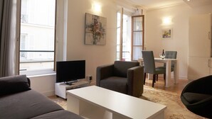 A modern living room with a flat-screen TV, a sofa, a dining table with chairs, and artwork on the walls. - ETOILE, LIVELY, FRESH MARKET, 30–60 days ahead? Ask for a private offer. PON-VAp (Paris)
