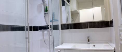 Un baño moderno con cabina de ducha de vidrio, un lavabo blanco y un espejo sobre él.