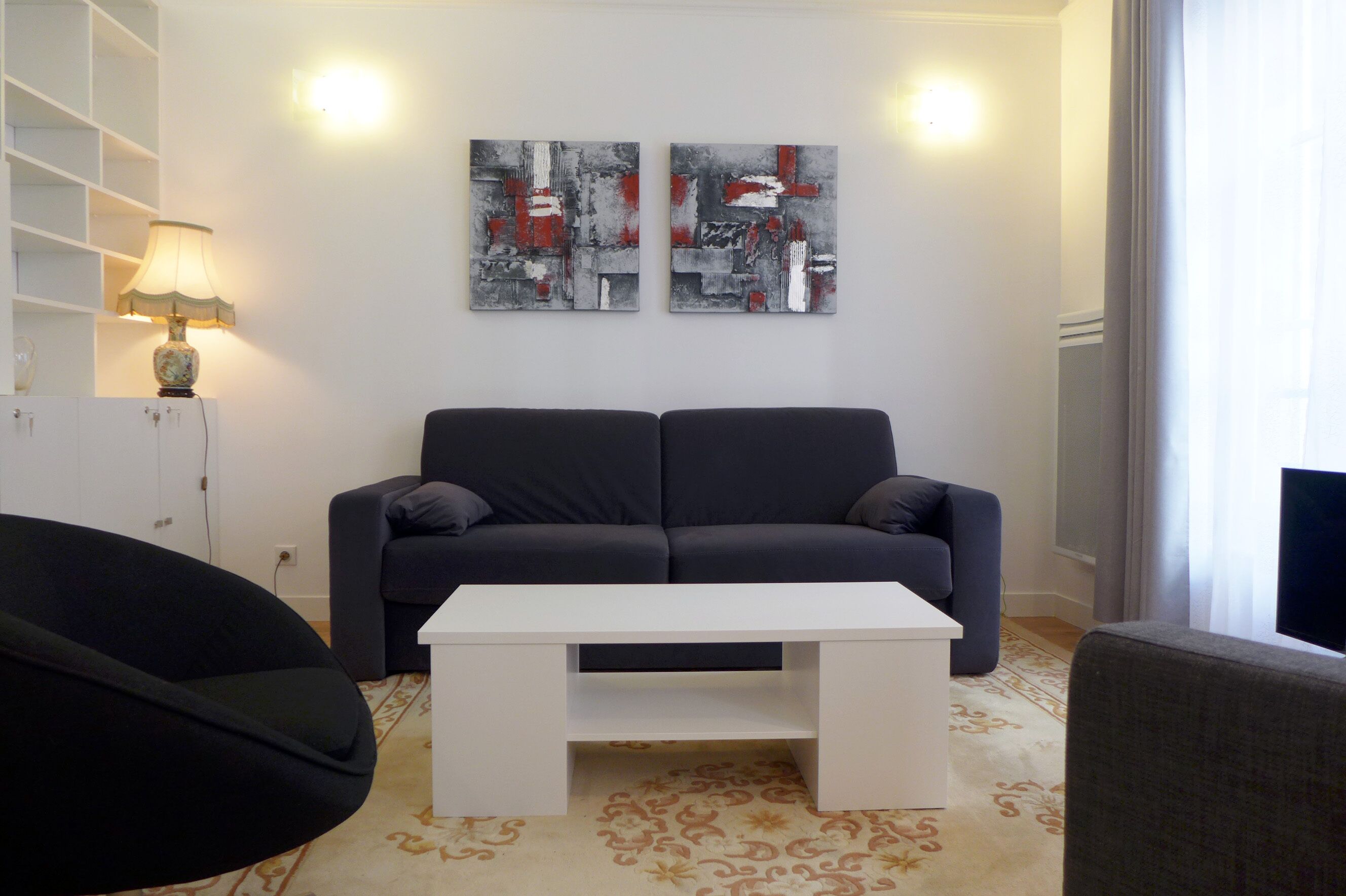 Una sala moderna con un sofá gris oscuro, una mesa de centro blanca y arte abstracto en la pared.