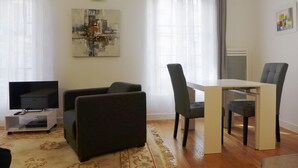 A living room with a flat-screen TV, a sofa, a dining table with chairs, and a rug. - ETOILE, LIVELY, FRESH MARKET, 30–60 days ahead? Ask for a private offer. PON-VAp (Paris)