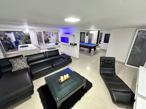 A living room with a pool table, black leather sofas, a glass coffee table, and a view of an outdoor area.