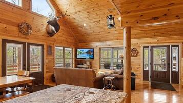 L’intérieur d’une cabane en rondins comprend un coin repas, un salon avec une cheminée et un téléviseur.