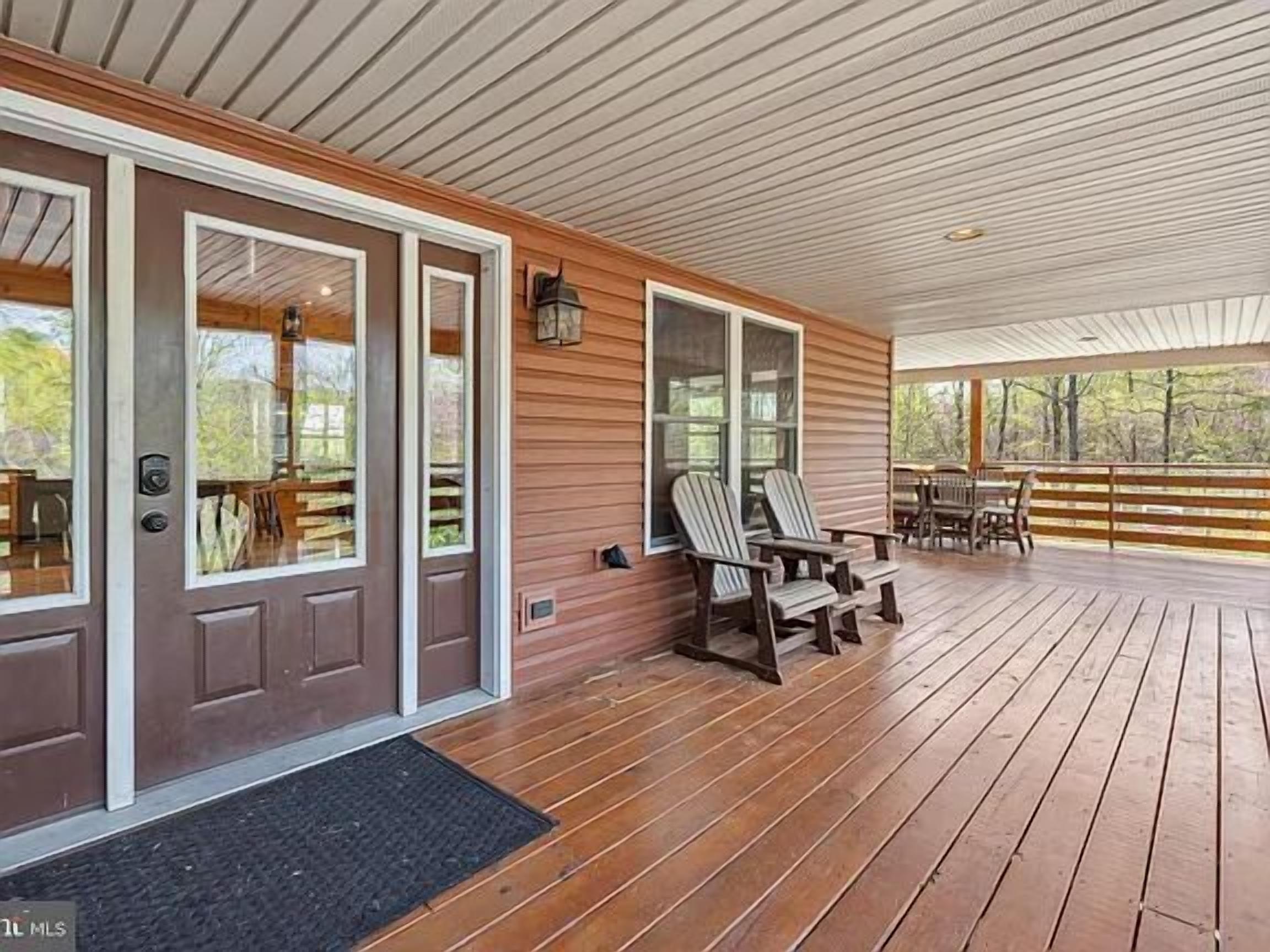 Une véranda couverte avec un plancher en bois, deux fauteuils Adirondack et une table.