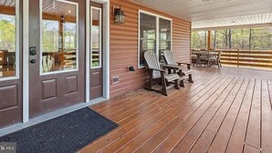 Un porche cubierto con piso de madera, dos sillas Adirondack y una mesa.