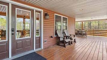 Une véranda couverte avec un plancher en bois, deux fauteuils Adirondack et une table.