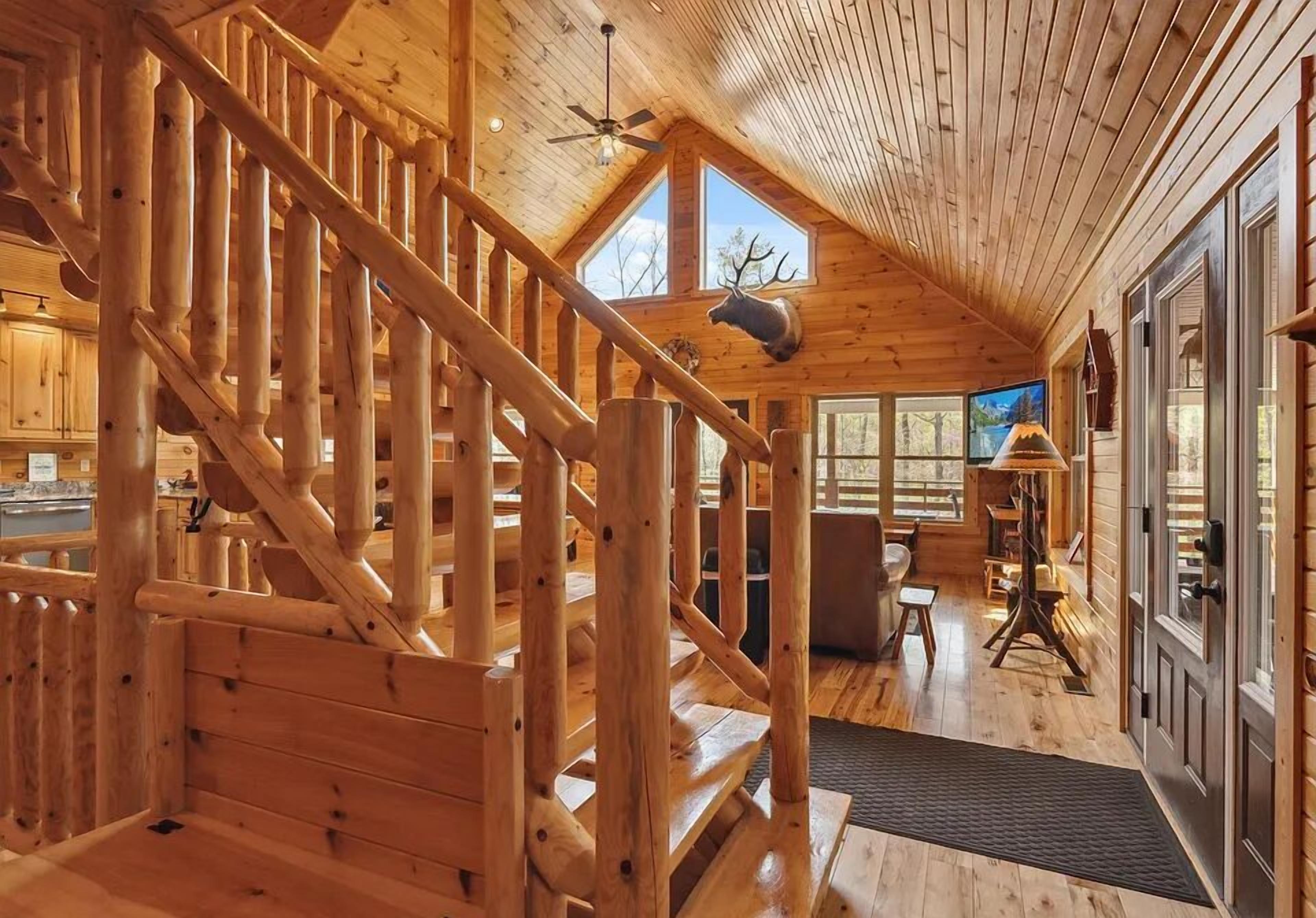 L’intérieur d’une cabane en bois, avec un escalier, un coin repas et une grande fenêtre.