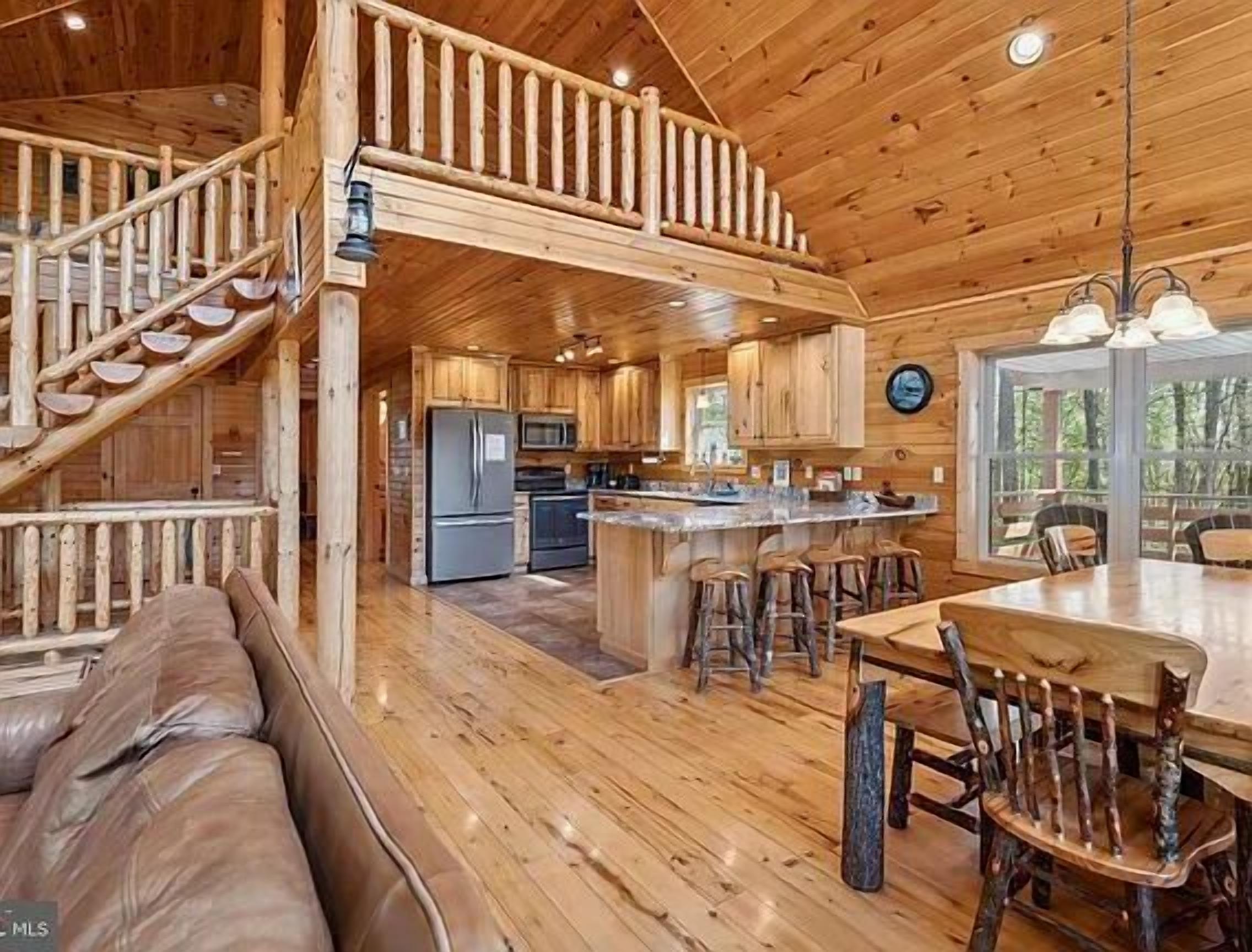 L’intérieur de la cabane comprend un escalier en bois, un coin cuisine, un espace repas avec une table et des chaises en bois, ainsi qu’un coin salon avec un canapé.