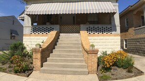 A two-story house with a front porch, brick steps, and a small garden with yellow flowers. - Adorable Loft Apartment (Wildwood Crest)