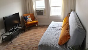 A living room with a TV, a sofa, a chair, and a window with curtains. - Adorable Loft Apartment (Wildwood Crest)