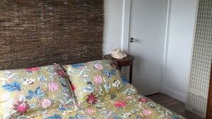 A room with a bed covered in a floral-patterned bedspread, a wooden headboard, a white door, and a small table with a decorative item. - Adorable Loft Apartment (Wildwood Crest)