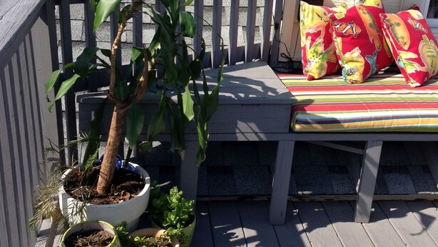 A wooden deck with a bench and colorful cushions, surrounded by potted plants. - Adorable Loft Apartment (Wildwood Crest)