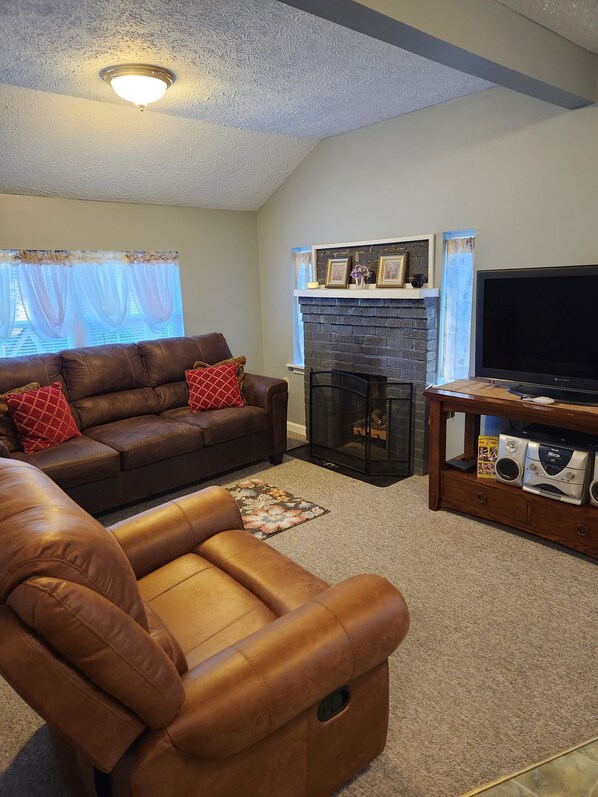 A living room with a brown leather sofa, a brown leather chair, a fireplace, a television, and a wooden entertainment unit.