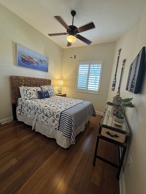 A bedroom with a bed, a ceiling fan, a window with blinds, a nightstand, a lamp, a plant, and a framed picture on the wall. - ALL 5 STAR REVIEWS for our 2Br.Cottage at Naples Bay Resort (Naples)