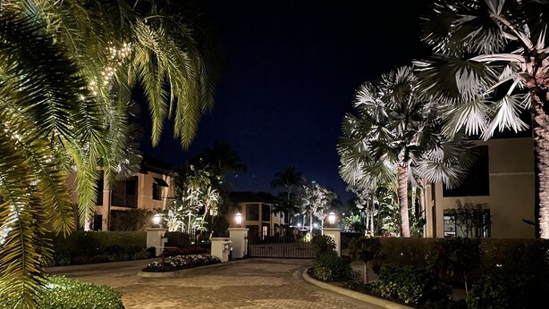 Vista nocturna de un complejo turístico con senderos pavimentados, palmeras y edificios iluminados.