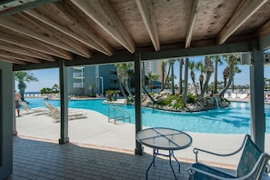 Un área de piscina techada con sillones, una mesa y vistas a un edificio con balcones.