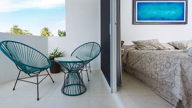Un balcon avec un lit, deux chaises, une table et un tableau.