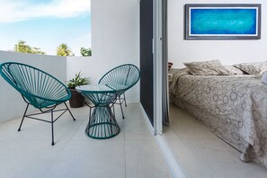 Un balcon avec un lit, deux chaises, une table et un tableau.