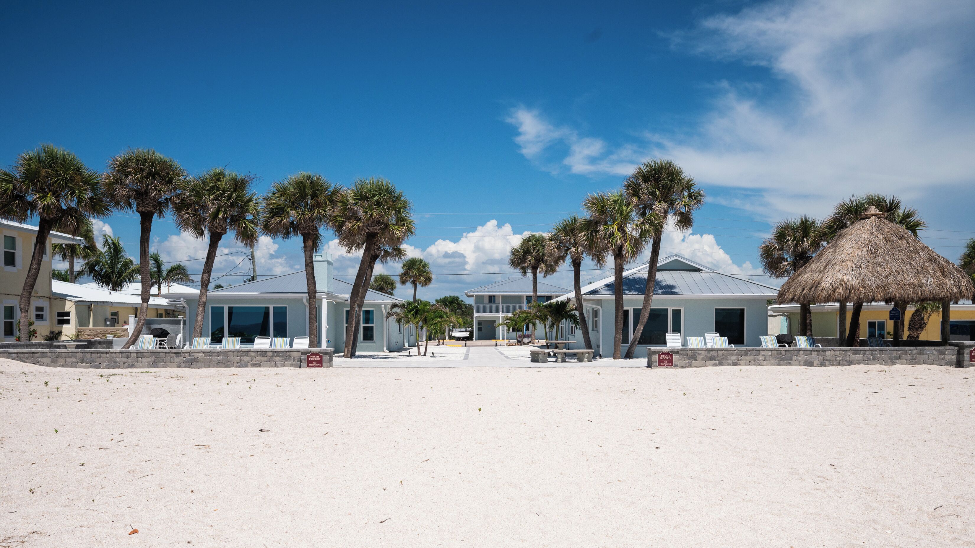 Ein Strandhotel mit mehreren Zimmern, Palmen und einer Struktur mit Reetdach.