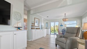A spacious living area with a large window, a grey armchair, and a flat-screen TV mounted on the wall. - One Bedroom remodeled stand-alone Unit - steps from our private beach. (Nokomis)