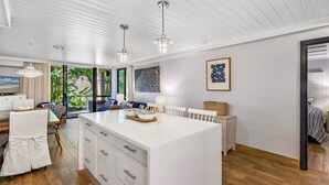 Cozinha moderna com uma ilha grande, armários brancos e iluminação pendente.