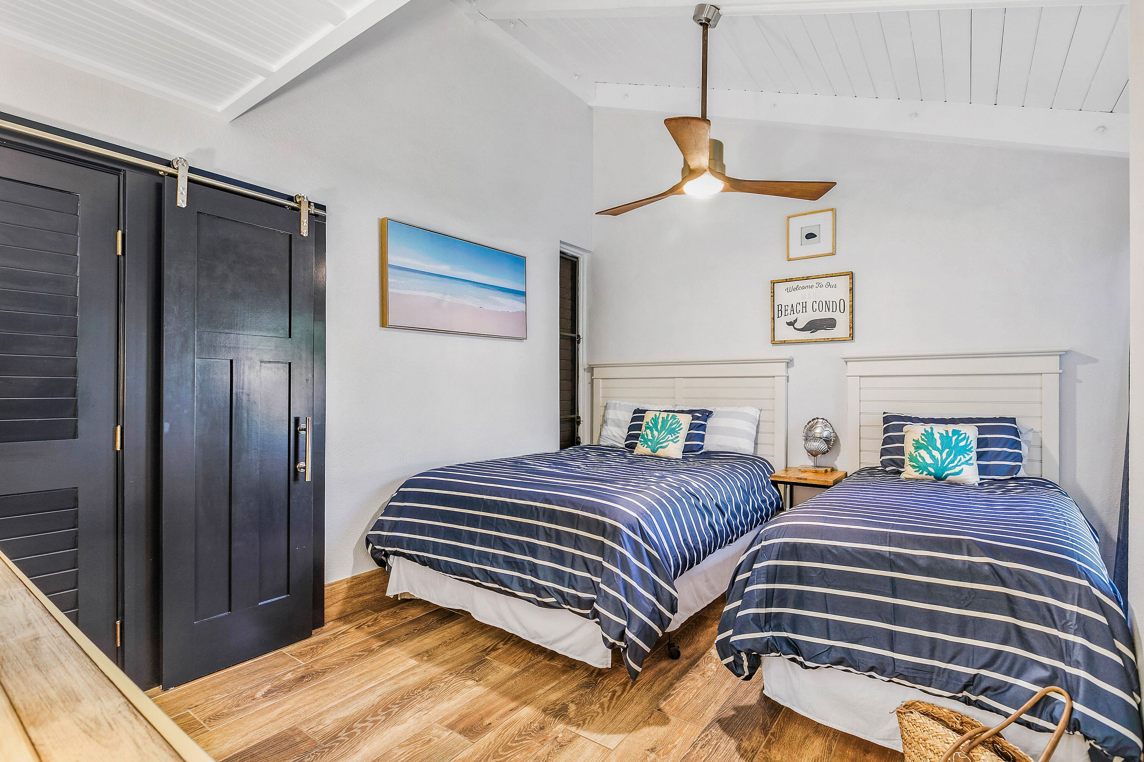 Un dormitorio con dos camas, ventilador de techo y decoración temática playera.
