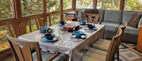 Comedor con una mesa dispuesta para cuatro personas, rodeado de sillas de madera y un sofá.