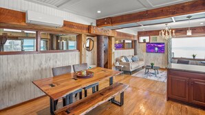 Uma sala de jantar espaçosa com uma mesa de madeira e bancos, uma área de estar aconchegante com um sofá e poltronas, e uma cozinha com armários de madeira.