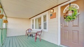 A covered porch with a table and chairs, a door with a wreath, and a window with a sign. - Year-Round Hampton Beach Retreat-3BR Beach Ranch w/Central A/C, Heat & Parking (Hampton)