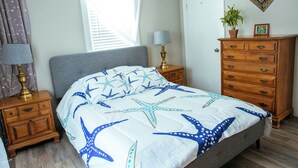 A bedroom with a bed, nightstands, a dresser, a window with blinds, and a wall-mounted mirror. - Year-Round Hampton Beach Retreat-3BR Beach Ranch w/Central A/C, Heat & Parking (Hampton)