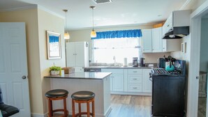 A kitchen with a central island, two bar stools, a refrigerator, and a window with blue curtains. - Year-Round Hampton Beach Retreat-3BR Beach Ranch w/Central A/C, Heat & Parking (Hampton)