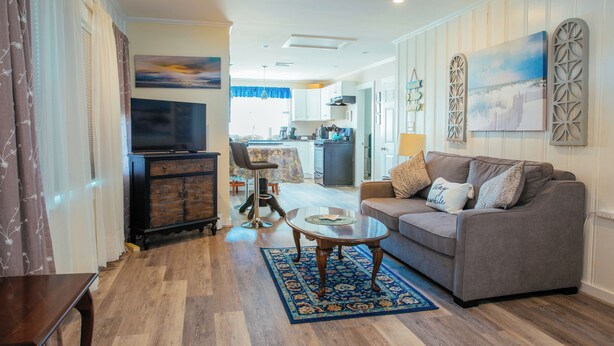 A living room with a sofa, coffee table, and TV. There is a kitchen in the background. - Year-Round Hampton Beach Retreat-3BR Beach Ranch w/Central A/C, Heat & Parking (Hampton)
