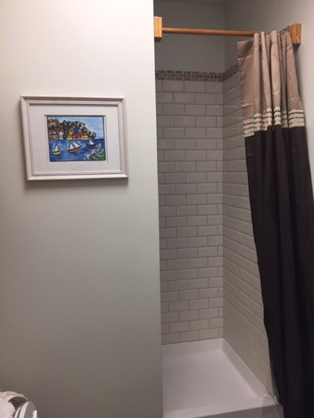 Ett badrum med dusch, en inramad tavla på väggen och en handduksställning.