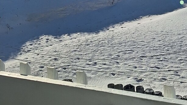 Una platja nevada amb un cel clar i un avió a la distància.