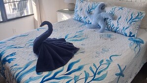 Un dormitori amb un llit amb llençols d'estil mar blau i blanc, un coixí amb forma de cigne i adhesius murals de estrelles de mar.